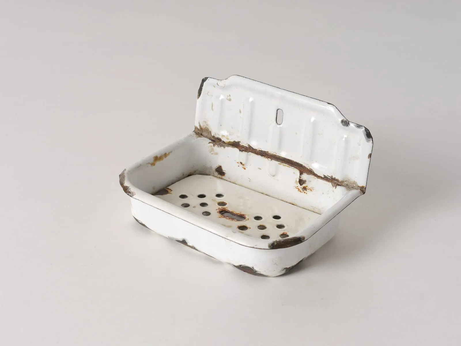 An old white enamel wall soap dish with drainage holes in its base.